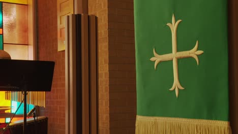 a close dolly shot of a cross crucifix church banner draped across a lectern altar inside a historic church as stained glass windows frame the background