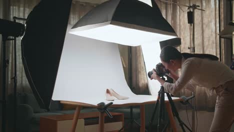 asian female photographer walking into home studio and taking photos of women's shoes