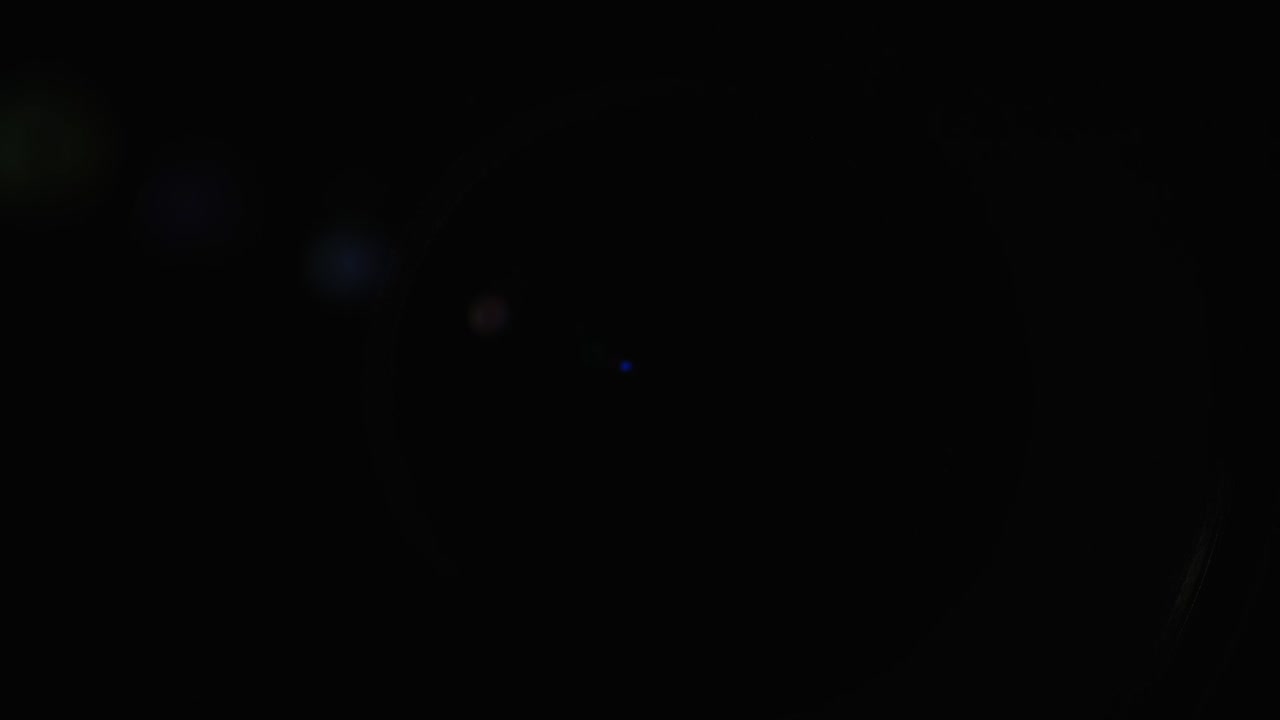 Un primo piano dell'obiettivo di una videocamera. La sorgente luminosa illumina le lenti, poi va nell'oscurità