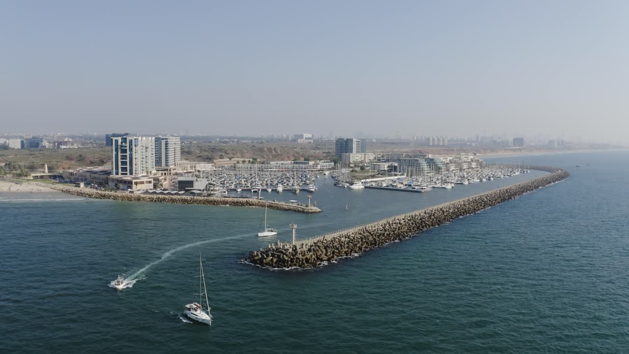 dos veleros blancos y una lancha de alta velocidad salen del puerto deportivo de herzeliya en israel mientras un windsurf navega por el mediterráneo a alta velocidad