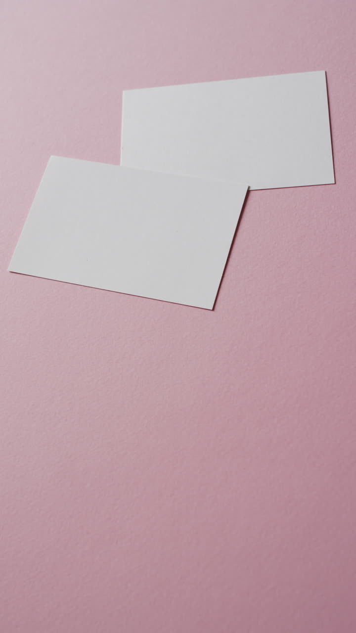 Vertical video of two blank white business cards on pink background, copy space, slow motion