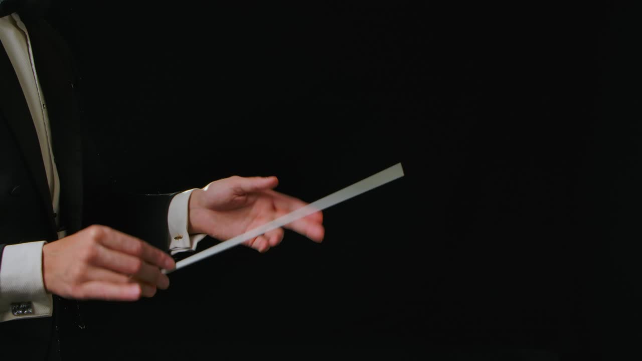 движущиеся руки дирижера оркестра, направляющего музыкантов с движением палки на черном фоне с огнями. дирижирование, направление классического музыкального исполнения с видимыми жестами. близко