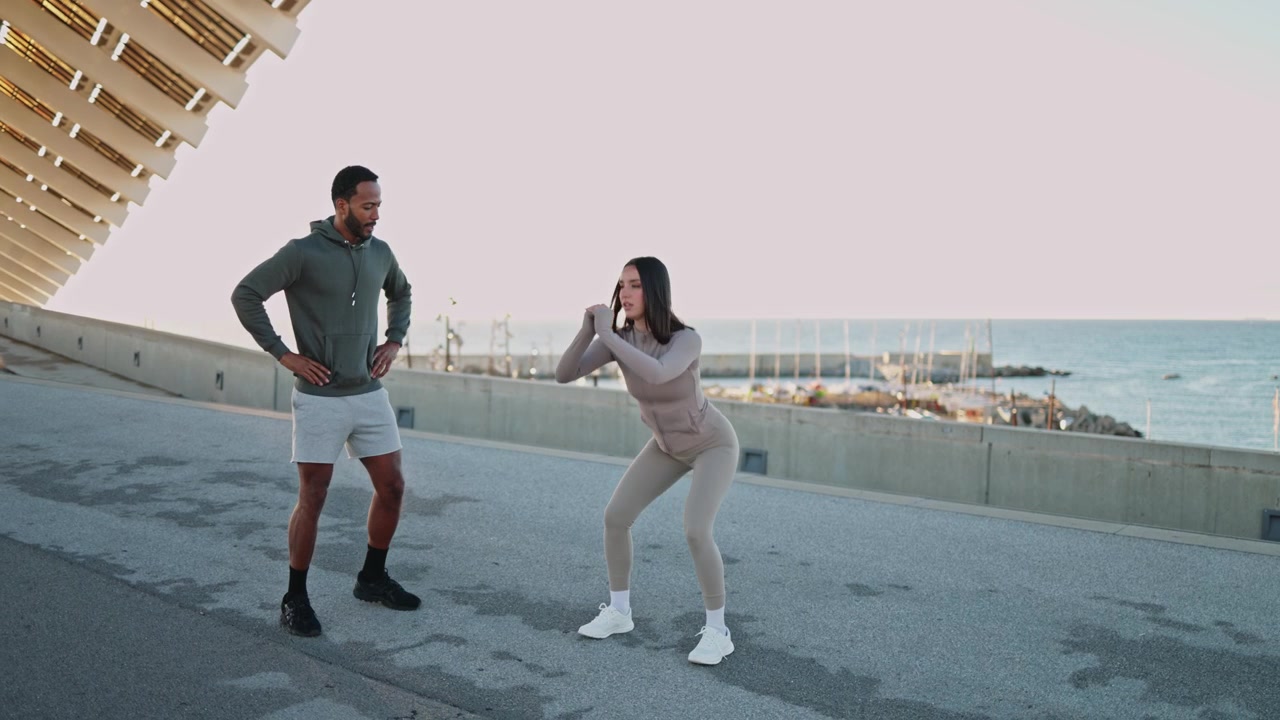 Personal trainer che allena una donna mentre fa squat all'aperto in riva al mare