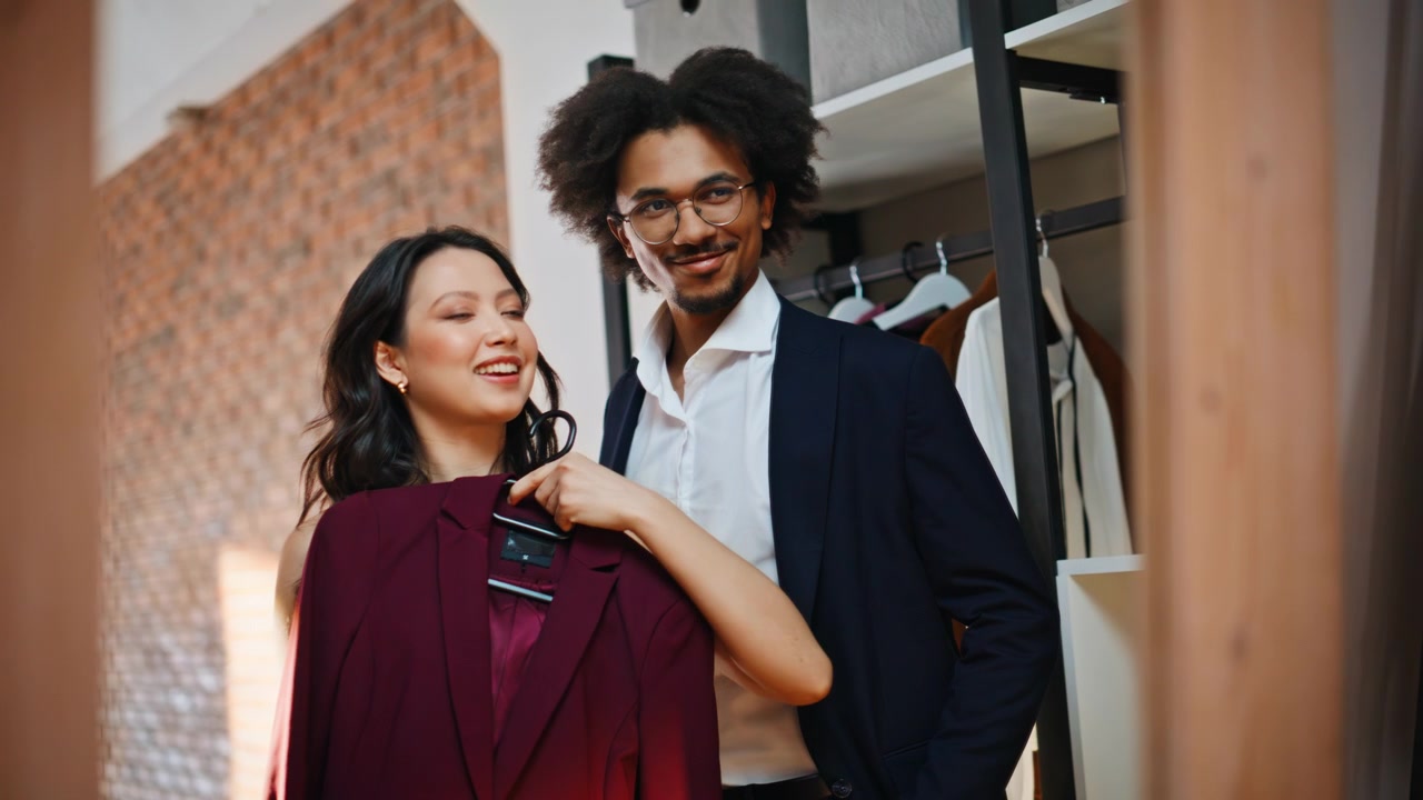 Retail partners choosing blazers wardrobe. Happy multiethnic team holds suits.