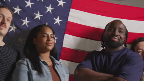 studio portrait shot of multi-cultural group of friends holding american flag behind them celebrating 4th july independence day 4