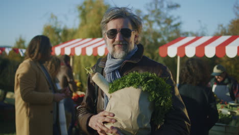 mature man in sunglasses posing with bag mature man in sunglasses posing with bag of fruits or vegetables and looks at camera shops on farmers market buys fresh products and takes care about health