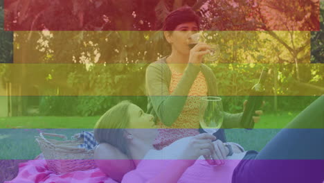 animation of pride rainbow stripes over happy caucasian lesbian couple drinking wine in sunny garden