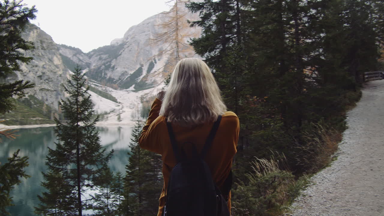 A blonde woman takes a photo of the landscape at Lake Braies in Italy