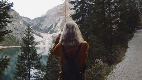 a blonde woman takes a photo of the landscape at lake braies in italy