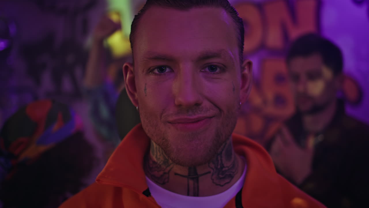 Tattooed man party neon glow looking camera defiantly closeup. Portrait clubber