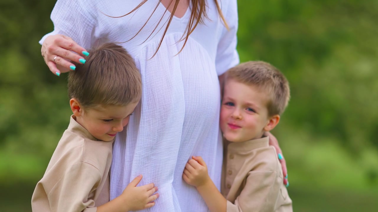 Zwei kleine Jungen umarmen und berühren den Bauch ihrer schwangeren Mutter.