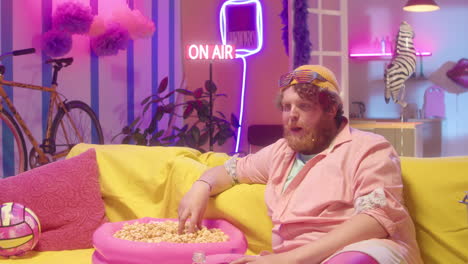 man eating popcorn in a neon-lit retro living room