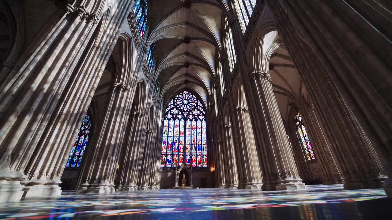 Toma de video en ángulo bajo del interior de una gran catedral, mostrando imponentes columnas y coloridas vidrieras.