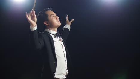 side view of asian conductor man holding a baton closing his eyes and showing gesture in the black studio