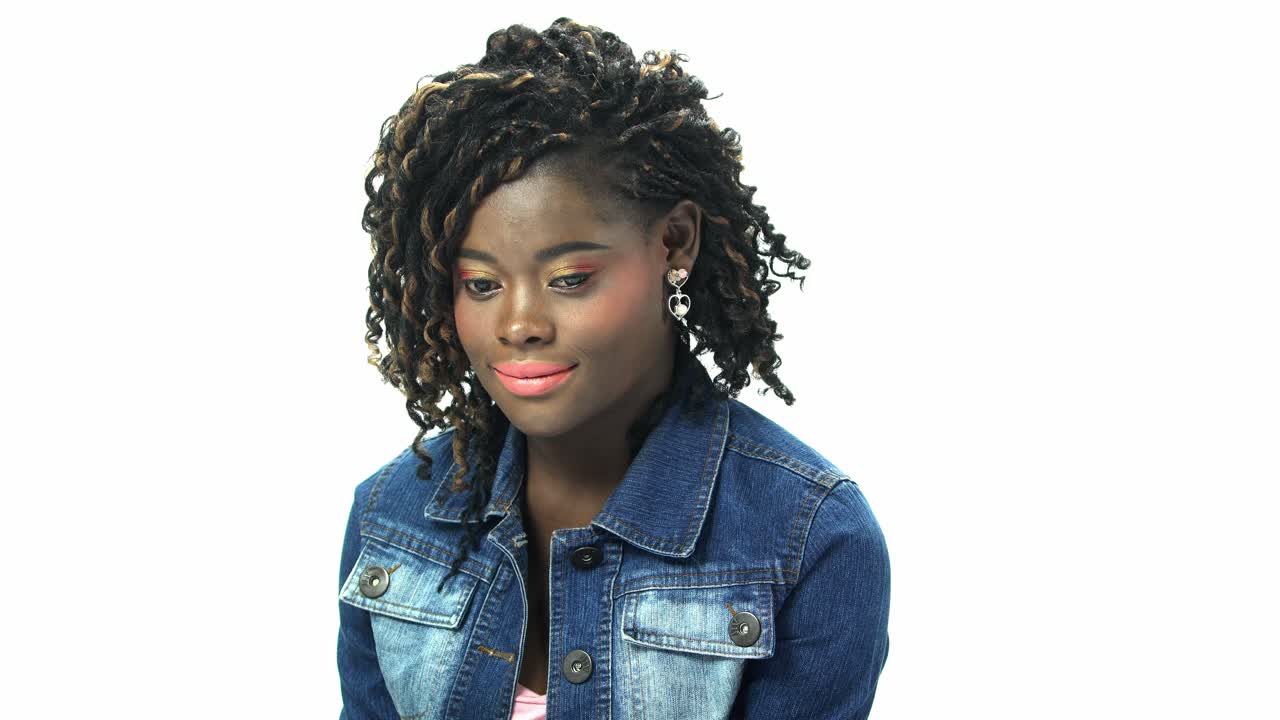 Giovane donna afroamericana ventenne con capelli afro neri e truccata, in t-shirt e giacca di jeans, esprime emozione su sfondo bianco per casting di clip virali o pubblicità.