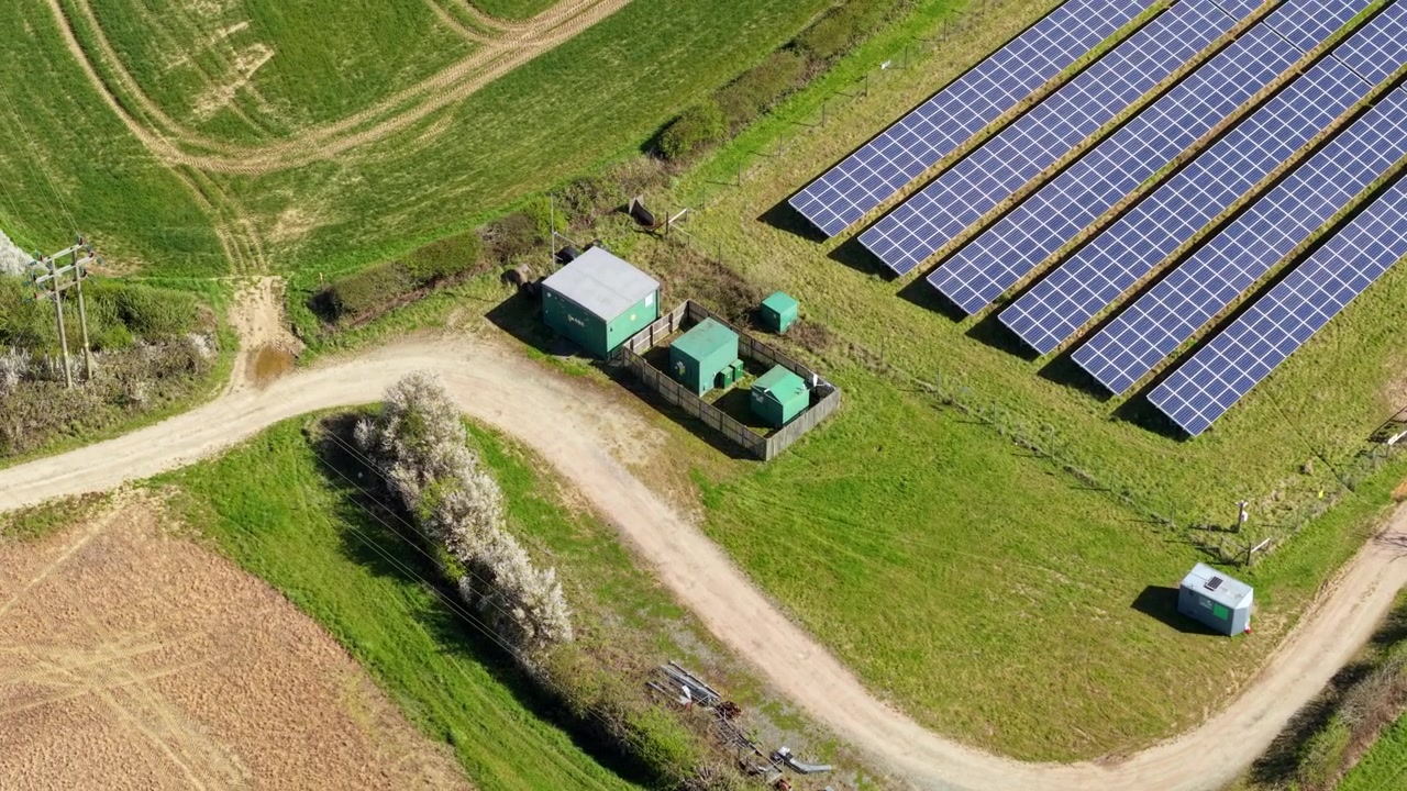 Luftfoto af solcellepark og containerbaseret strøminverter-konverterstation.
