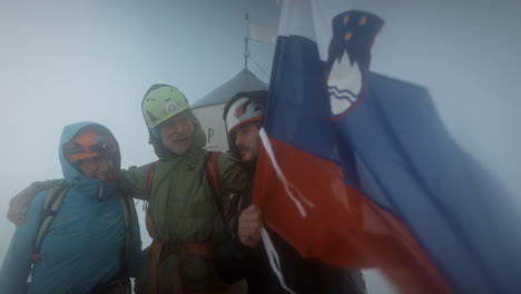 excursionistas con cascos posando frente a la torre aljaž ondeando con bandera eslovena