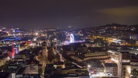 moving aerial night time lapse in 4k of downtown skyline in the city of stuttgart, germany from left to right with ferris wheel.