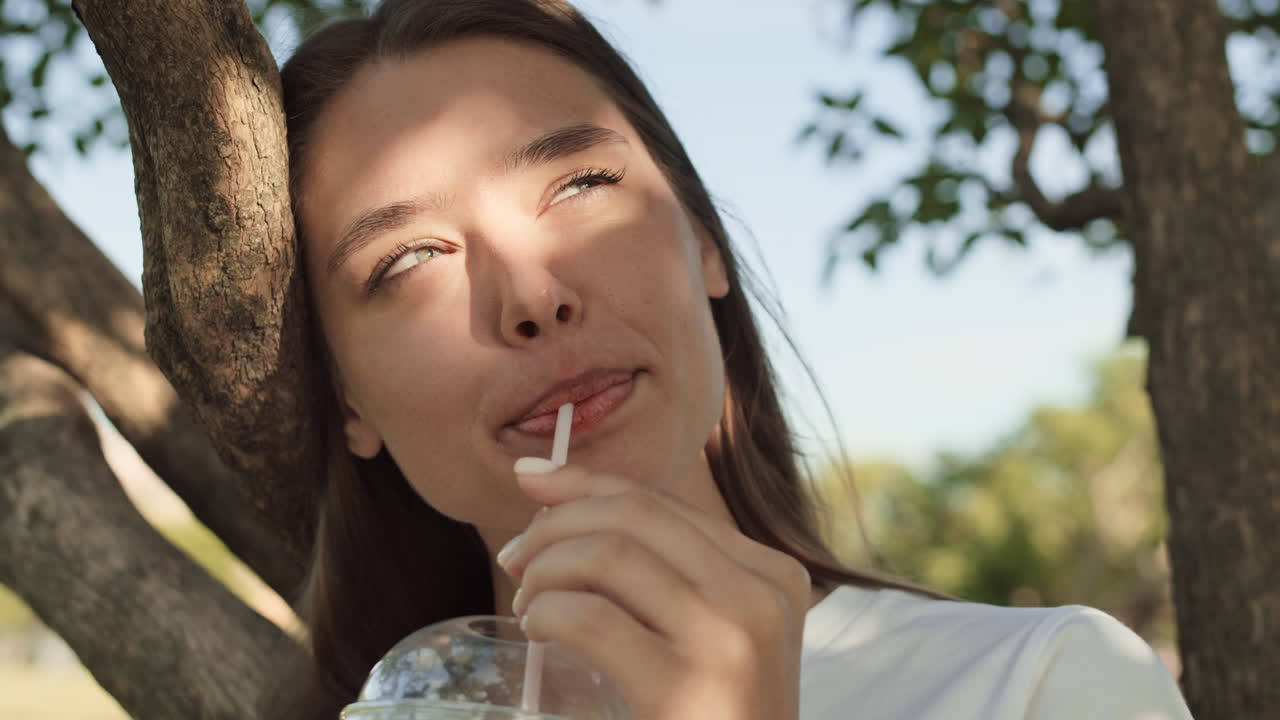 Woman Drinking Beverage Leaning on Tree