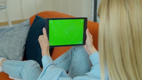 una chica bonita haciendo una llamada de video en una tableta digital. una mujer en casa usa una tableta virtual de pantalla verde. está sentada en un sofá en su acogedora sala de estar.