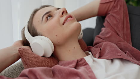 young woman relaxing on a couch, listening to music with headphones