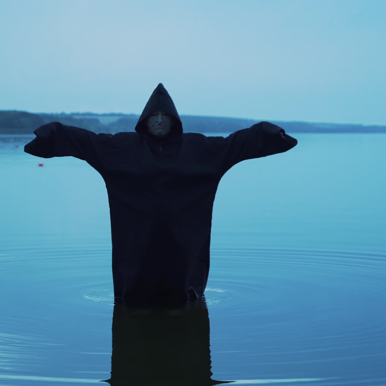 Evil witch in black cloak with hood in the river. Halloween costume.