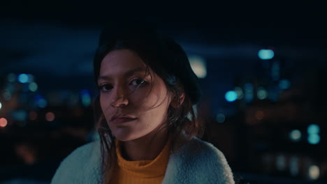 portrait of beautiful young mixed race woman on rooftop at night looking serious with bokeh city lights in urban skyline background