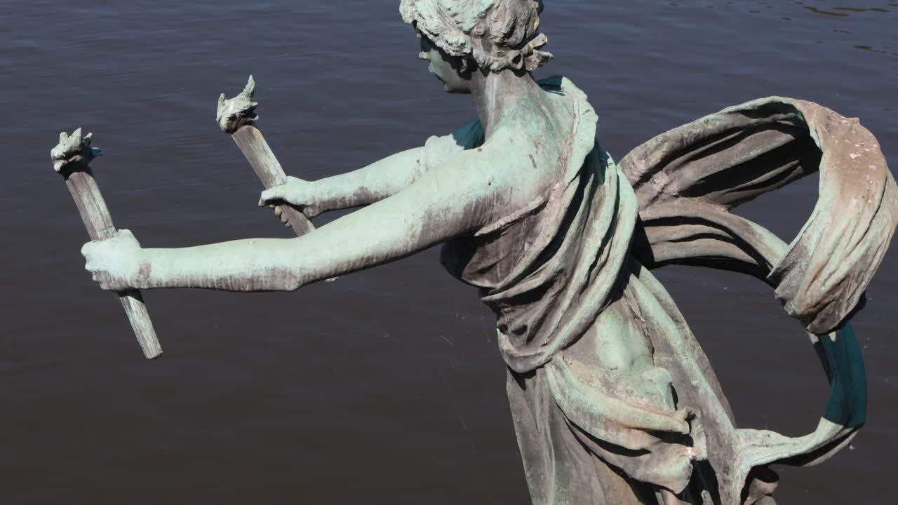 Side view of bronze classical female statue with torch, slow camera pan above river surface