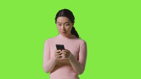 studio shot of woman checking mobile phone and getting good news message against green screen