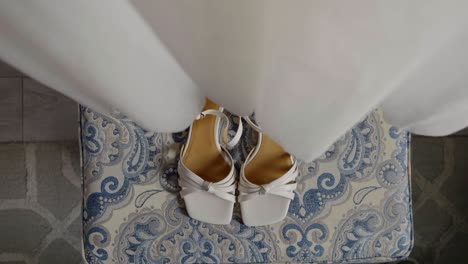 a flowing white wedding dress made of delicate fabric with white shoes placed underneath. the bride's preparations for her big wedding day
