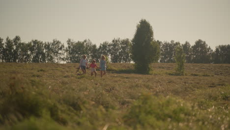 dog owner holding dog leash walking alongside mother and daughter in vast grassy field on sunny day, all three stroll leisurely through rural landscape, with trees and open sky in background