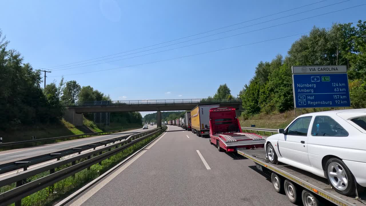 Multiple cargo trucks and vehicles drive along a sunny highway, captured from a moving perspective