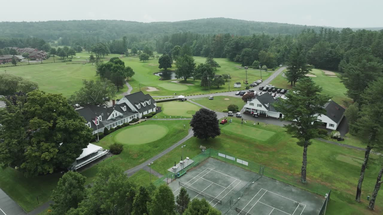 Aerial view of Augusta Country Club in Maine, showing clubhouse, tennis courts, and lush golf course set against a backdrop of rolling forested hills.