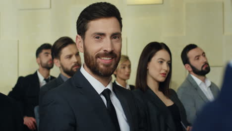 caucasian mature businessman sitting on a chair among people in a conference room, then he turns his face to the camera and smiling