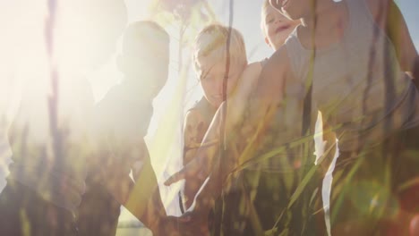 Animation-of-sun-and-grasses-over-happy-diverse-schoolchildren-stacking-hands-in-outdoor-sport-class