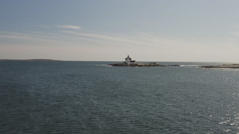 waves lapping a small rocky island with a white lighthouse, coast of maine, aerial