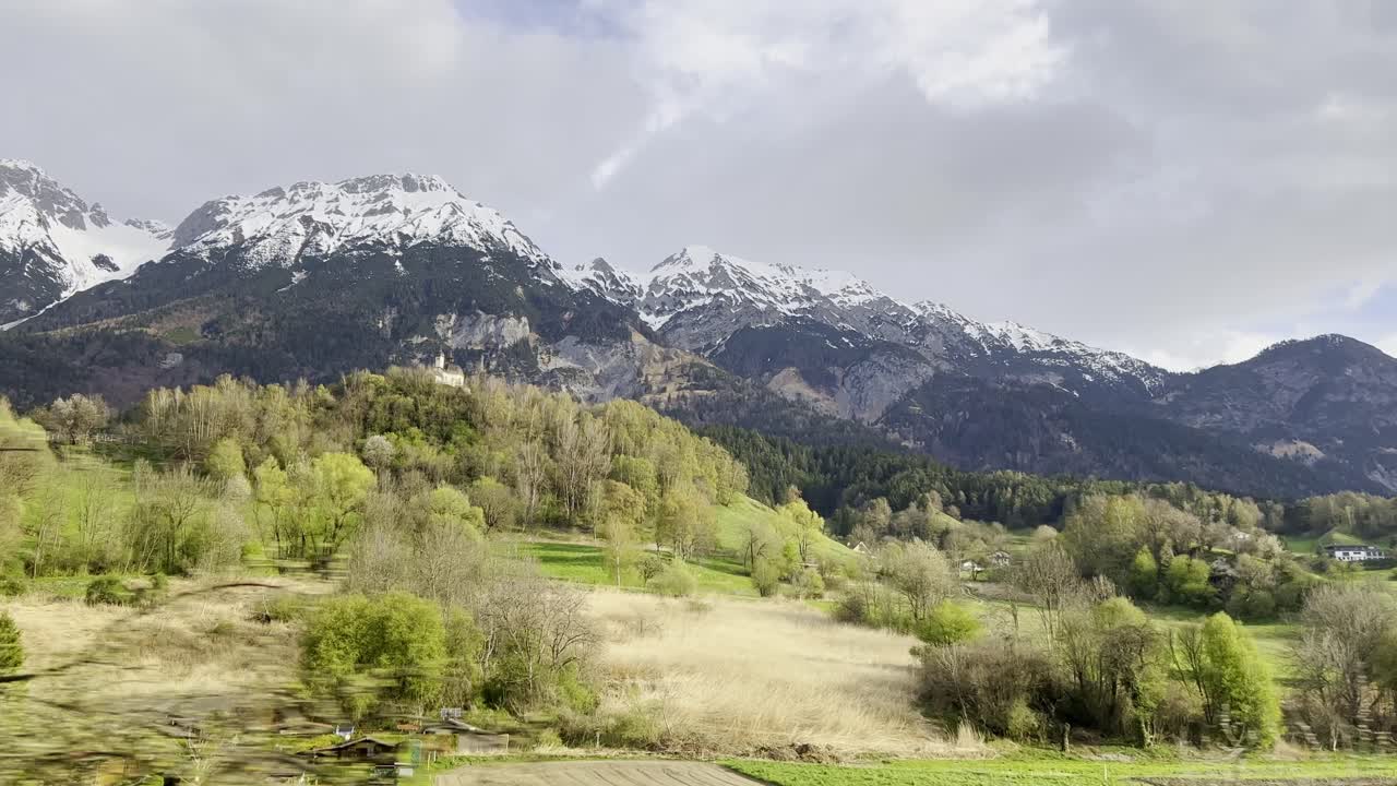 vista desde la ventana del tren pasando majestuosas montañas cubiertas de nieve que se elevan sobre exuberantes valles verdes