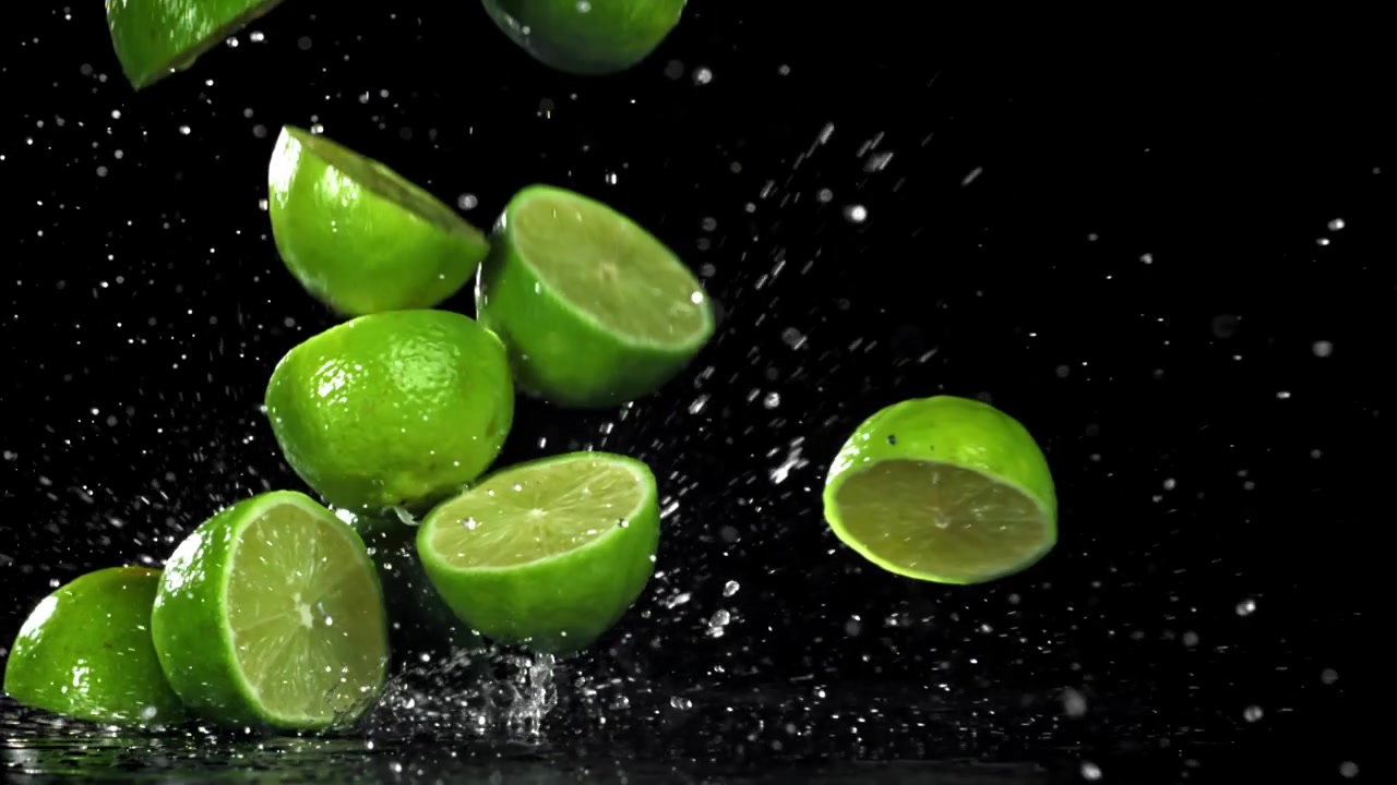Friske limefrugter og halve limefrugter falder ned i vand med plask i slowmotion