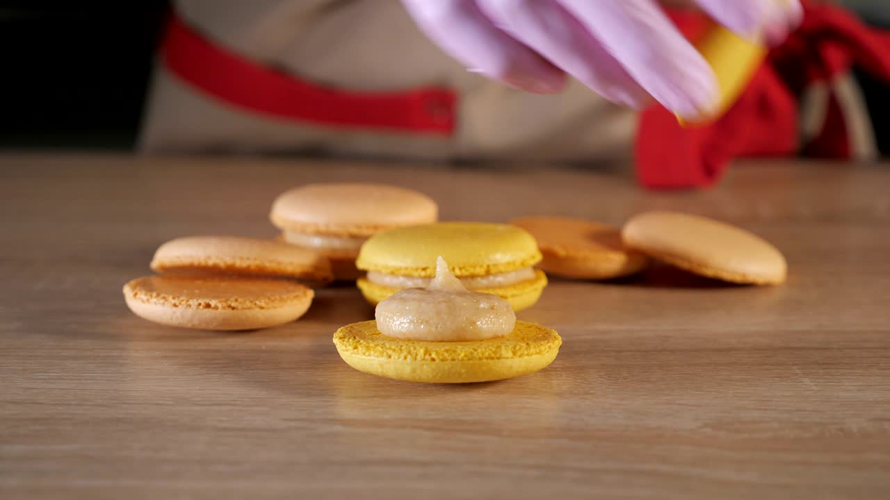 el chef de pastelería está llenando macarrones de limón con crema usando una bolsa de dulces.
