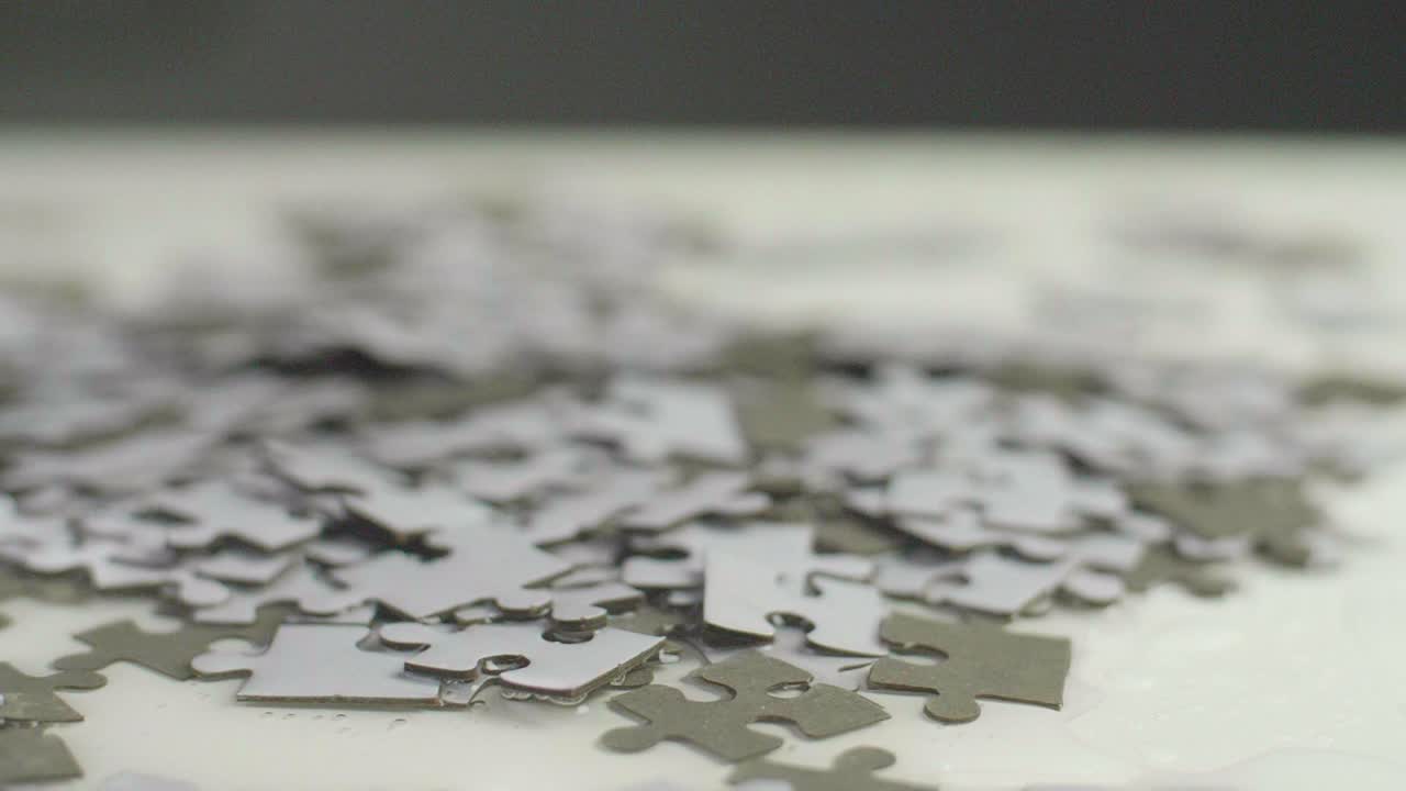 Slow motion of water dripping on white and gray puzzle pieces laying randomly on a white surface. Shot in 4K;  Shallow depth of field. Smooth camera sliding movement.