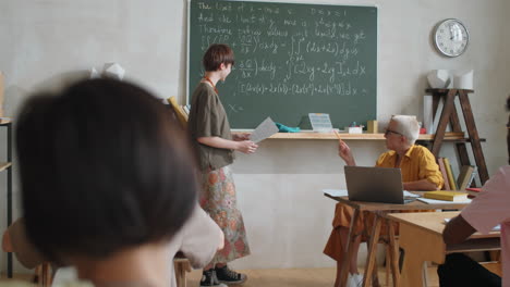 Cheerful-Female-Student-Standing-by-Chalkboard-and-Talking-on-Lesson