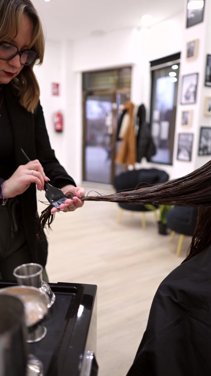 Parrucchiere professionista che applica la tinta per capelli a una cliente in salone