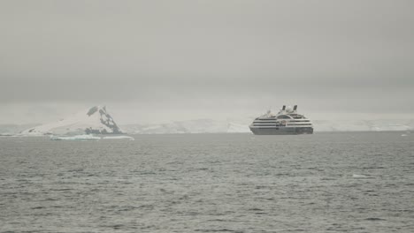 Big-cruise-expedition-ship-going-through-icebergs-along-coastline-with-glaciers-snow-and-ice