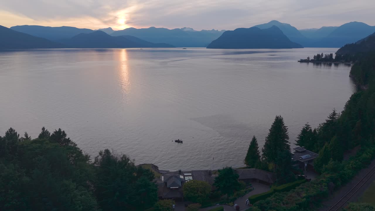 an aerial drone shot with the sunsetting over Gambier Island, with a single boat on the coast of Lions Bay with luxury properties in the foreground