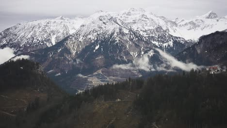 Amidst-gloomy-clouds,-an-aerial-perspective-reveals-the-Austrian-Alps-adorned-with-a-delicate-layer-of-snow-on-their-dark-peaks