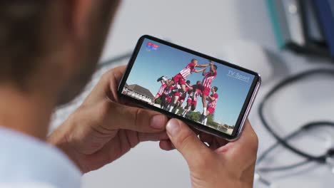compuesto de un médico masculino viendo un evento deportivo en un teléfono inteligente