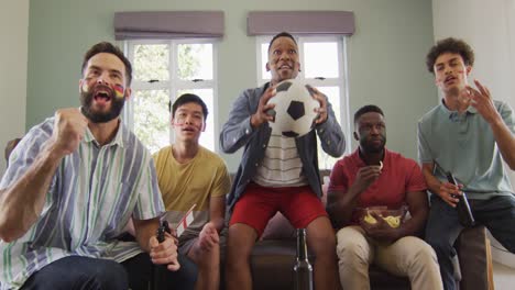 happy diverse male friends watching tv and drinking beer in living room