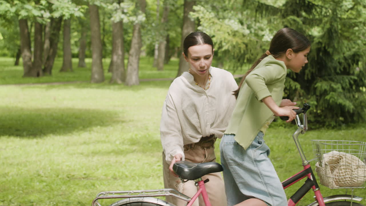 Girl learning to ride a bike with help from her mother in a park