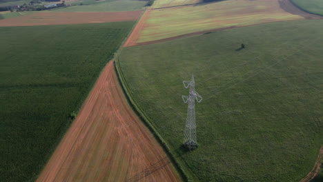 aerial view of high voltage tower surrounded by plowed fields of peasants in the italian countryside during sunset in northern italy - aerial drone shot
