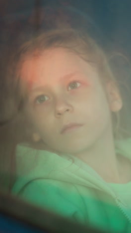 upset child sits in car on rainy day. frustrated little girl looks at falling rain out of auto window at riding. preschooler kid bored of long road trip